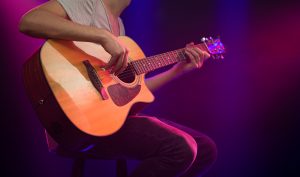The musician plays an acoustic guitar. Beautiful background with colored light rays. The concept of music and playing a musical instrument.